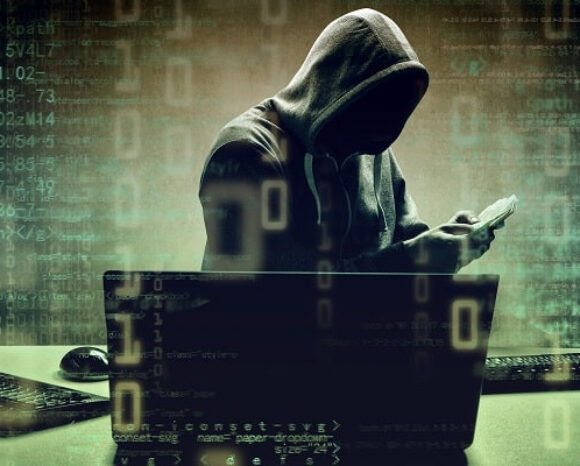 Eine vermummte Gestalt in einem schwach beleuchteten Raum, umgeben von Laptops, auf denen Codes und Zahlen angezeigt werden. Die bedrohliche Atmosphäre deutet auf Cyberkriminalität hin und erinnert an die berüchtigte LAPSUS$-Bande. Die Gestalt untersucht aufmerksam ein Mobilgerät und ist tief in ihre geheimen Aktivitäten vertieft.