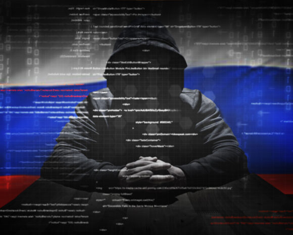 Eine Person in einem Kapuzenpullover sitzt mit gefalteten Händen an einem Tisch. Überall sind Codezeilen zu sehen. Im Hintergrund ist die russische Flagge zu sehen, die mit einem digitalen Matrix-Motiv verschmilzt und auf die drohende Präsenz von Advanced Persistent Threats (APTs) hindeutet.