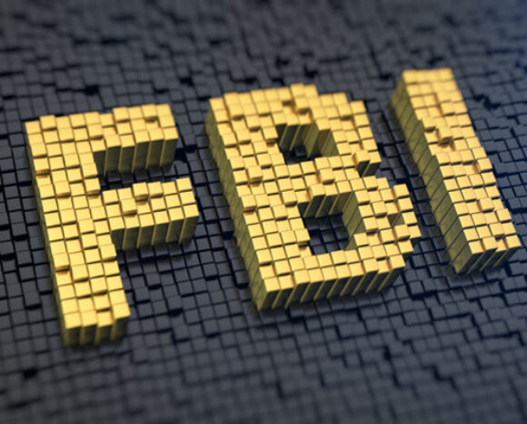Das Bild zeigt „FBI“ in dreidimensionalen goldenen Blockbuchstaben auf einem strukturierten dunklen Hintergrund aus kleinen schwarzen Würfeln und symbolisiert Autorität angesichts digitaler Herausforderungen wie Hackback.