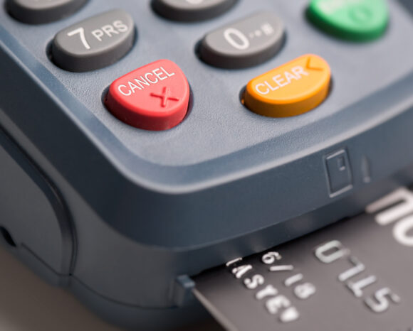 Nahaufnahme eines Zahlungsterminals mit Fokus auf den Schaltflächen „Abbrechen“ und „Löschen“, die sicheres Identitätsmanagement verdeutlichen. Eine Kreditkarte ist teilweise in den Schlitz des Geräts eingeschoben, was auf eine laufende Transaktion schließen lässt.