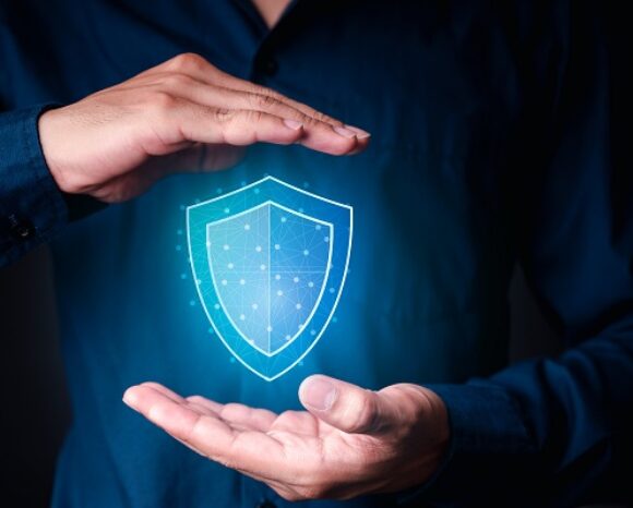 Eine Person in einem dunklen Hemd hält ihre Hände um ein leuchtendes digitales Schildsymbol. Das Symbol zeigt ein netzwerkartiges Muster und symbolisiert Cybersicherheit und Schutz. Dennoch muss man sich vor „falscher Sicherheit“ hüten – der Illusion vollständiger Sicherheit im digitalen Bereich.