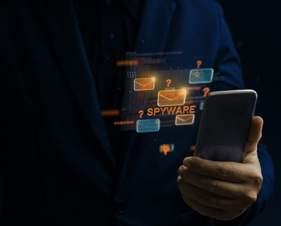 Eine Person im dunklen Anzug hält ein Smartphone. Holografische Bilder von Umschlägen, Fragezeichen und der orangefarbenen Schrift „SPYWARE-KAMPAGNEN“ schweben vor dunklem Hintergrund über dem Telefon und symbolisieren digitale Bedrohungen und Cybersicherheitsbedenken.