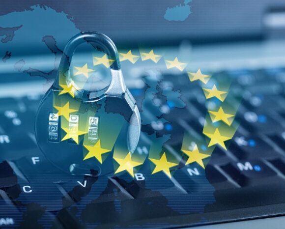 Auf einer Computertastatur befindet sich ein Vorhängeschloss mit Ziffernblatt, darüber eine Europakarte. Sterne umrahmen es wie die EU-Flagge und symbolisieren die Datensicherheit gemäß dem Digital Services Act der Europäischen Union.