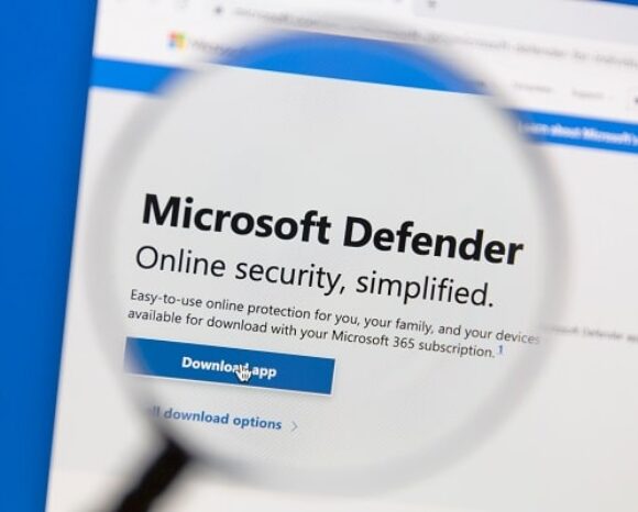 Über der Microsoft Defender-Webseite schwebt eine Lupe, die den Text „Online-Sicherheit, vereinfacht“ und eine blaue Schaltfläche „App herunterladen“ hervorhebt und Microsoft Virenschutz für 365-Benutzer präsentiert.