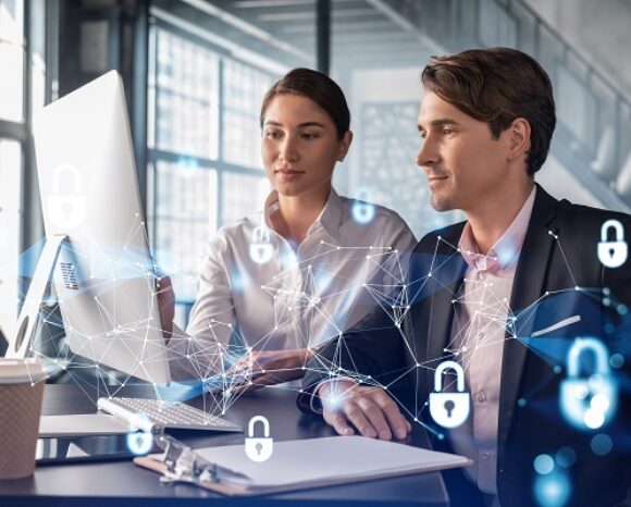 Mann und Frau arbeiten zusammen vor Laptop mit Cybersecurity-Symbolen