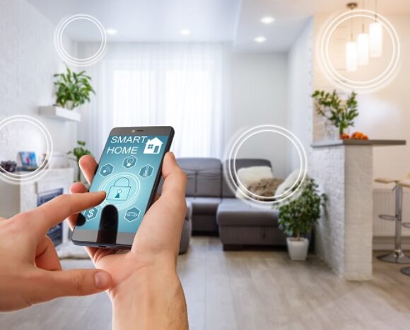 Eine Person nutzt ein Smartphone mit Smart-Home-Oberfläche in einem modernen Wohnzimmer. Der Bildschirm zeigt verschiedene Steuerungsmöglichkeiten für das Haus. Der Raum ist mit einem Sofa, Pflanzen, Barhockern und heller Beleuchtung ausgestattet. Digitale Kreise heben die Smart-Funktionen hervor.
