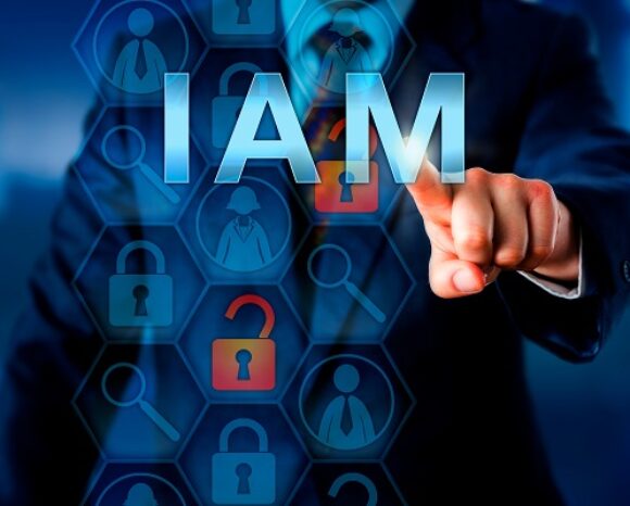Ein Fachmann im Anzug deutet auf die großen „IAM“-Schriftzüge auf einer digitalen Oberfläche, die an eine Webkonferenz erinnert. Der Hintergrund mit Symbolen von Vorhängeschlössern, Lupen und Personen unterstreicht das Thema Identity & Access Management im Bereich Sicherheit.