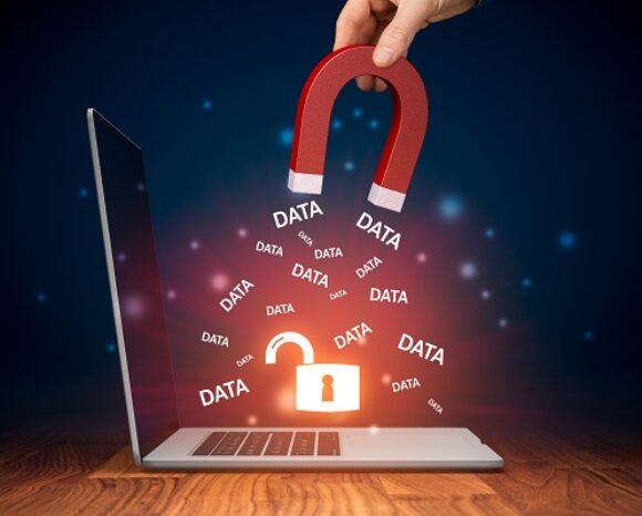 Eine Hand hält einen roten Magneten über einen Laptop-Bildschirm und zieht wiederholt das Wort „DATA“ in weißer Schrift. Darunter symbolisiert ein geschlossenes Schloss-Symbol Sicherheit vor Bedrohungen wie Keyloggern. Der Hintergrund ist dunkel, Leuchteffekte heben die Elemente hervor.