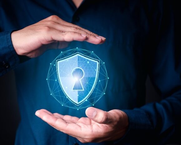 Eine Person in einem dunklen Hemd hält ihre Hände um ein leuchtendes digitales Schild mit einem Schlüsselloch in der Mitte, das Cybersicherheit und Datenschutz symbolisiert.