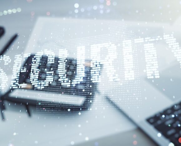 Das Bild zeigt das Wort „SECURITY“ in digitaler Schrift vor einem unscharfen Hintergrund mit Laptop und Dokumenten und symbolisiert damit Cybersicherheit. Punkte und Linien suggerieren Datenkonnektivität und deuten subtil auf höhere Investitionen in IT-Sicherheit für verbesserten Schutz hin.