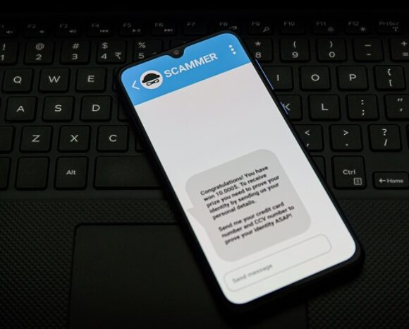 Auf einem Smartphone auf einer Tastatur wird eine Chat-App-Nachricht mit dem Titel „SCAMMER“ angezeigt. Die Nachricht, typisch für Cyberbetrüger, die mittlerweile über Twitter und Direktnachrichten kursieren, gratuliert dem Empfänger und fordert ihn auf, persönliche Daten und Kreditkarteninformationen preiszugeben, um einen fiktiven Geldpreis zu gewinnen.