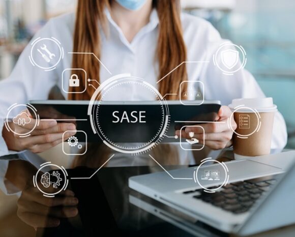Eine Person mit einem Tablet, auf dem ein „SASE“-Diagramm abgebildet ist, umgeben von Sicherheits- und Konnektivitätssymbolen wie einem Schloss und einem Schild, verkörpert die Essenz von „Mit SASE überall sehr einfach sichere Verbindungen schaffen“. In der Nähe ergänzen ein Laptop und eine Kaffeetasse die Szene, während die maskierte Person konzentriert bleibt.