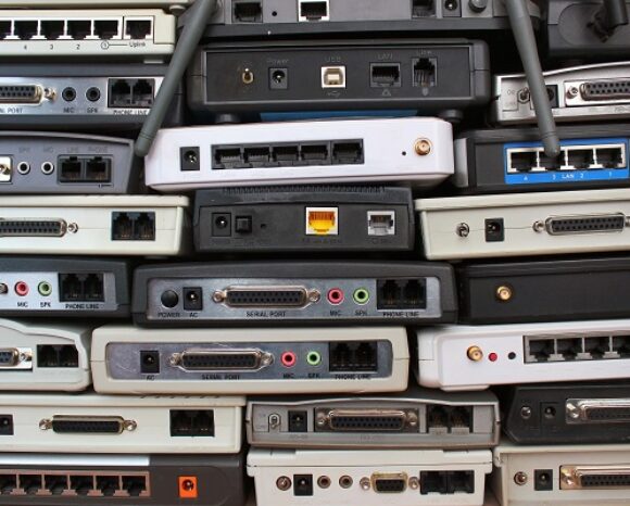 Eine Sammlung ausgemusterter Unternehmensrouter als Datenschleuder bietet eine Vielzahl von Anschlüssen und Konnektoren, darunter Ethernet-, serielle und Audio-Buchsen. Die Geräte variieren in der Farbe, meist in Schwarz und Grau, mit einigen weißen Modellen.