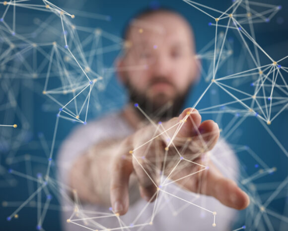 Inmitten eines virtuellen Netzwerks aus miteinander verbundenen Linien und Punkten streckt eine Person vor blauem Hintergrund die Hand aus. Die Szene deutet auf die Interaktion mit digitaler oder abstrakter Technologie hin, wobei Out-of-Band-Tools eine entscheidende Rolle spielen. Der Fokus liegt auf der Hand und dem unscharfen Hintergrund.