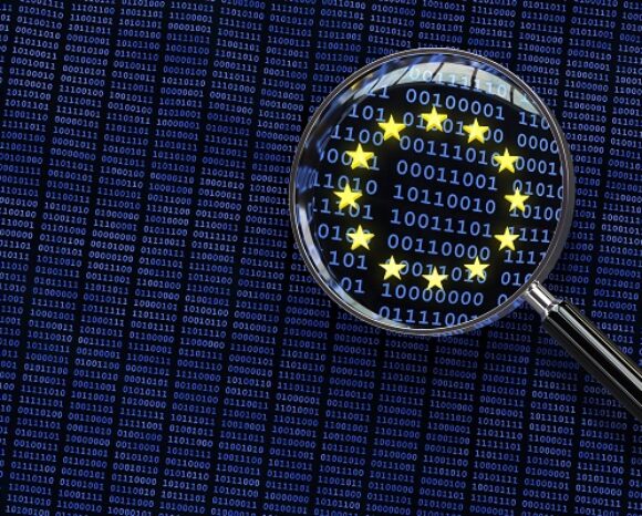 Eine Lupe vergrößert einen Abschnitt eines Binärcodes vor einem dunkelblauen Hintergrund und hebt die kreisförmig angeordneten Sterne hervor, die wie die Flagge der Europäischen Union aussehen und die darin verschlüsselte Nachricht „DSGVO: EU-Kommission verpasst Chance“ symbolisieren.