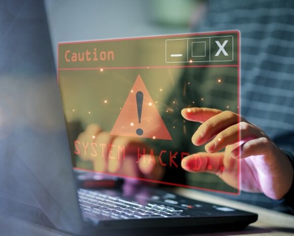 Eine Person tippt auf einem Laptop mit holografischem Bildschirm. Unter dem Hinweis „Vorsicht!“ erscheint ein rotes Warnschild mit der Aufschrift „SYSTEM GEHACKT!“. Ergänzt wird das Ganze durch die erschreckende Entdeckung von 100 schädlichen Treibern. Die Szene veranschaulicht anschaulich die drohende Gefahr von Cybersicherheitsbedrohungen.