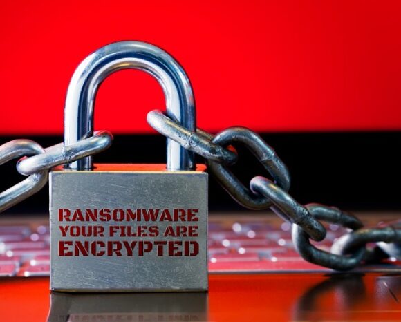 Auf einer Tastatur vor einem roten Hintergrund liegt ein Vorhängeschloss mit Ketten. Auf dem Schloss steht „RANSOMWARE, IHRE DATEIEN SIND VERSCHLÜSSELT“, was an Drohungen erinnert, die dem jüngsten Ransomware-Angriff auf MGM Resorts ähneln.