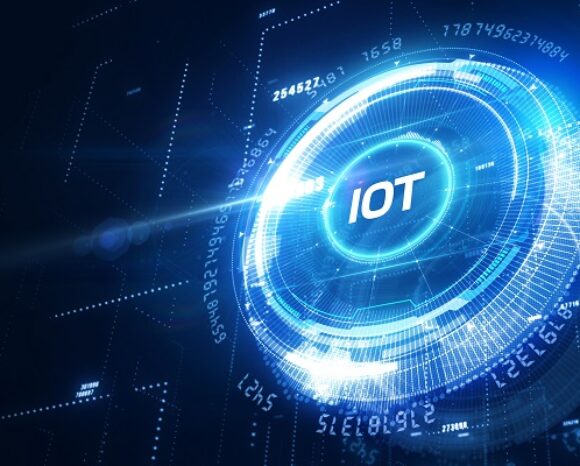 Futuristische digitale Grafik mit einer leuchtend blauen kreisförmigen Oberfläche, die in der Mitte den Text „IoT“ zeigt und veranschaulicht, wie „Wie sich das IoT unternehmensgerecht sichern lässt“, umgeben von abstrakten technologischen Elementen auf dunklem Hintergrund.