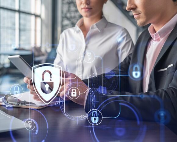 Mann und Frau vor Laptop. Im Vordergrund Datenschutzsymbol