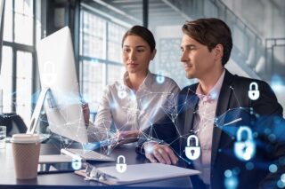Mann und Frau arbeiten zusammen vor Laptop mit Cybersecurity-Symbolen