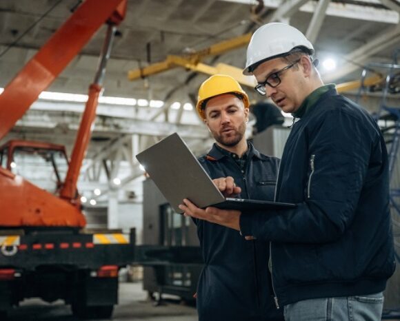 Zwei Männer in einer Industrieanlagen schauen in einen Laptop - OT-Security