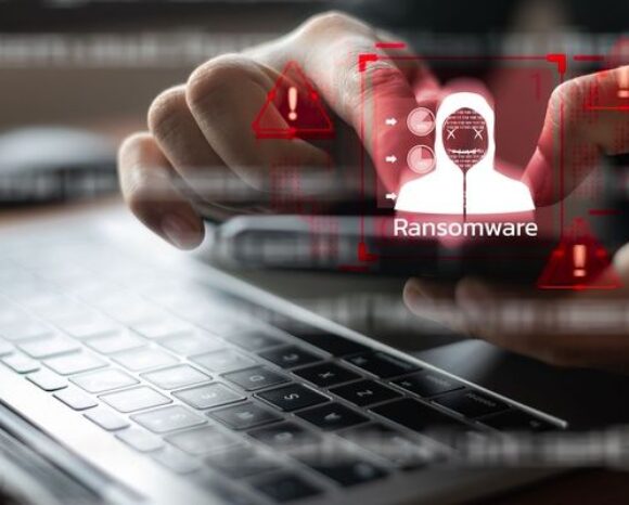 Person hält Smartphone mit roter Ransomware-Warnung und Sicherheitsalarm-Symbol über Laptop-Tastatur, Konzept für mobile Cybersecurity-Bedrohungen