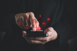 Smartphone mit holographischer Cybersecurity-Warnung und roten Sicherheitssymbolen vor dunklem Hintergrund