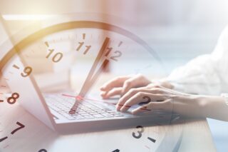 Tippende Hände auf Computertastatur und darüber eine Uhr, die Fünf vor Zwölf anzeigt