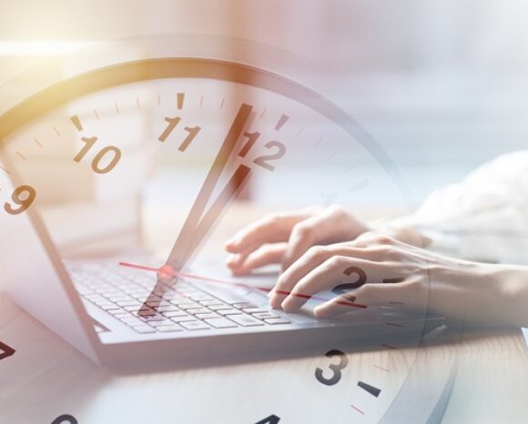 Tippende Hände auf Computertastatur und darüber eine Uhr, die Fünf vor Zwölf anzeigt