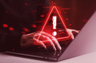 Cybersicherheitswarnung auf Laptop-Bildschirm mit tippenden Händen in dunkelroter Umgebung