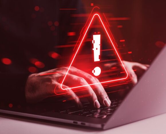 Cybersicherheitswarnung auf Laptop-Bildschirm mit tippenden Händen in dunkelroter Umgebung