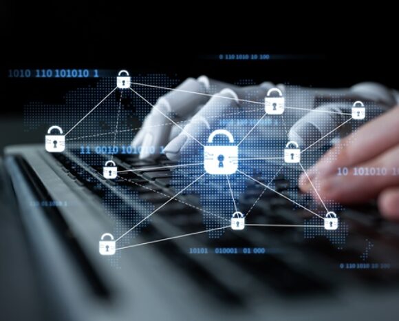 KI- und menschliche Hand tippend auf der Tastatur mit Cybersecurity-Symbol
