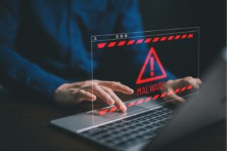 Rote Malware-Warnung auf dem Laptop-Bildschirm, während Hände tippen; Hinweis auf Cybersecurity-Risiko und IT-Sicherheitsvorfall am Schreibtisch.