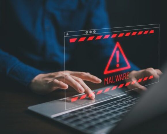Rote Malware-Warnung auf dem Laptop-Bildschirm, während Hände tippen; Hinweis auf Cybersecurity-Risiko und IT-Sicherheitsvorfall am Schreibtisch.